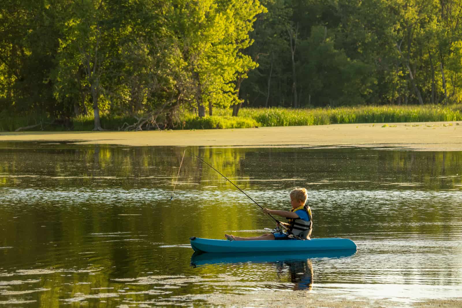 A child wearing a life jacket paddling a small kayak on a calm lake