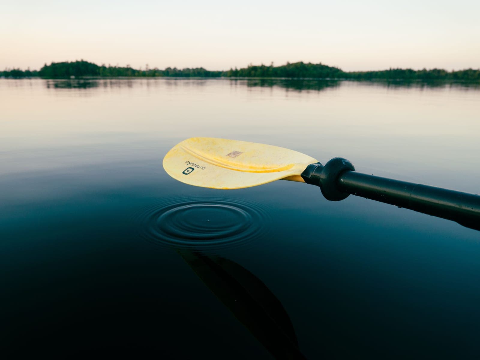 A kayak paddle blade entering calm water