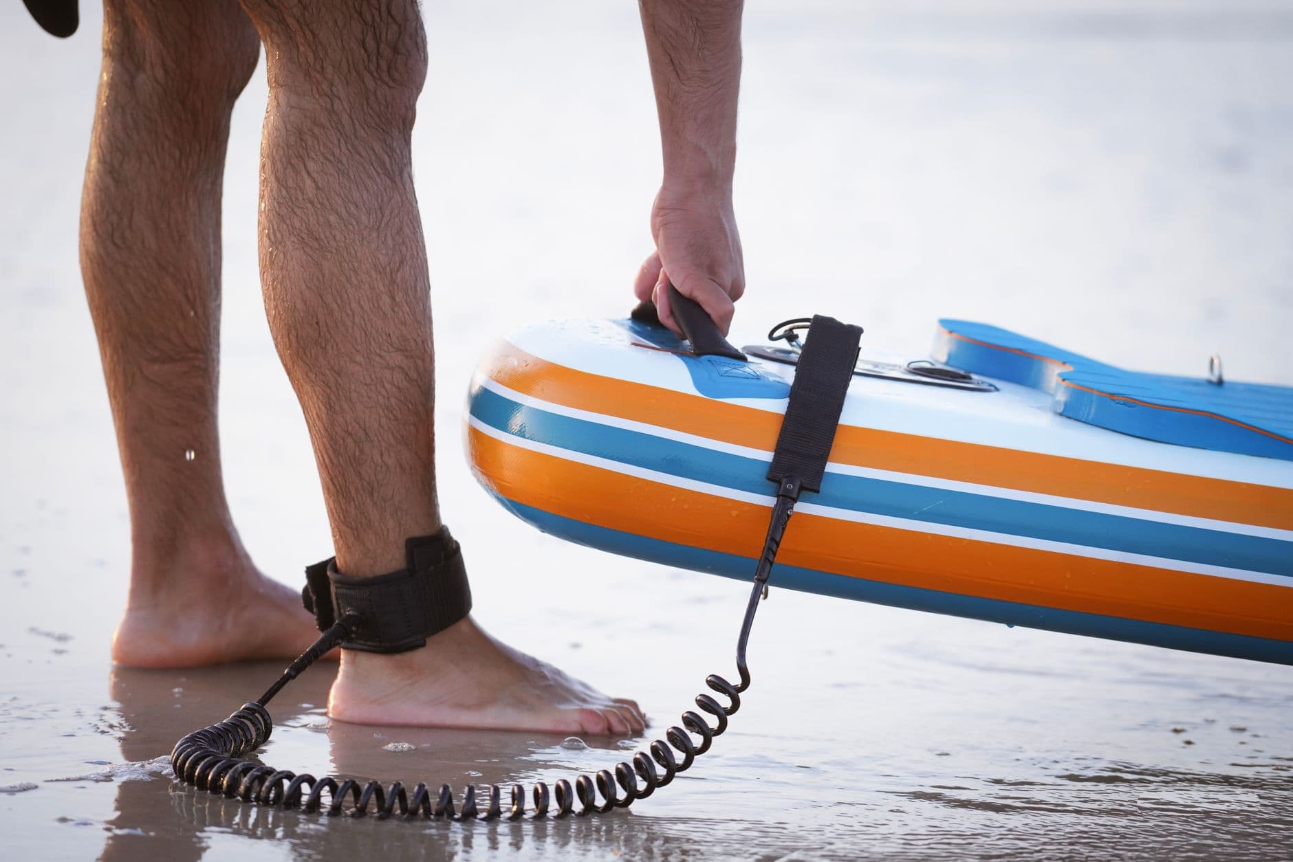 A paddler on the sand with a paddle board leash attached to their leg