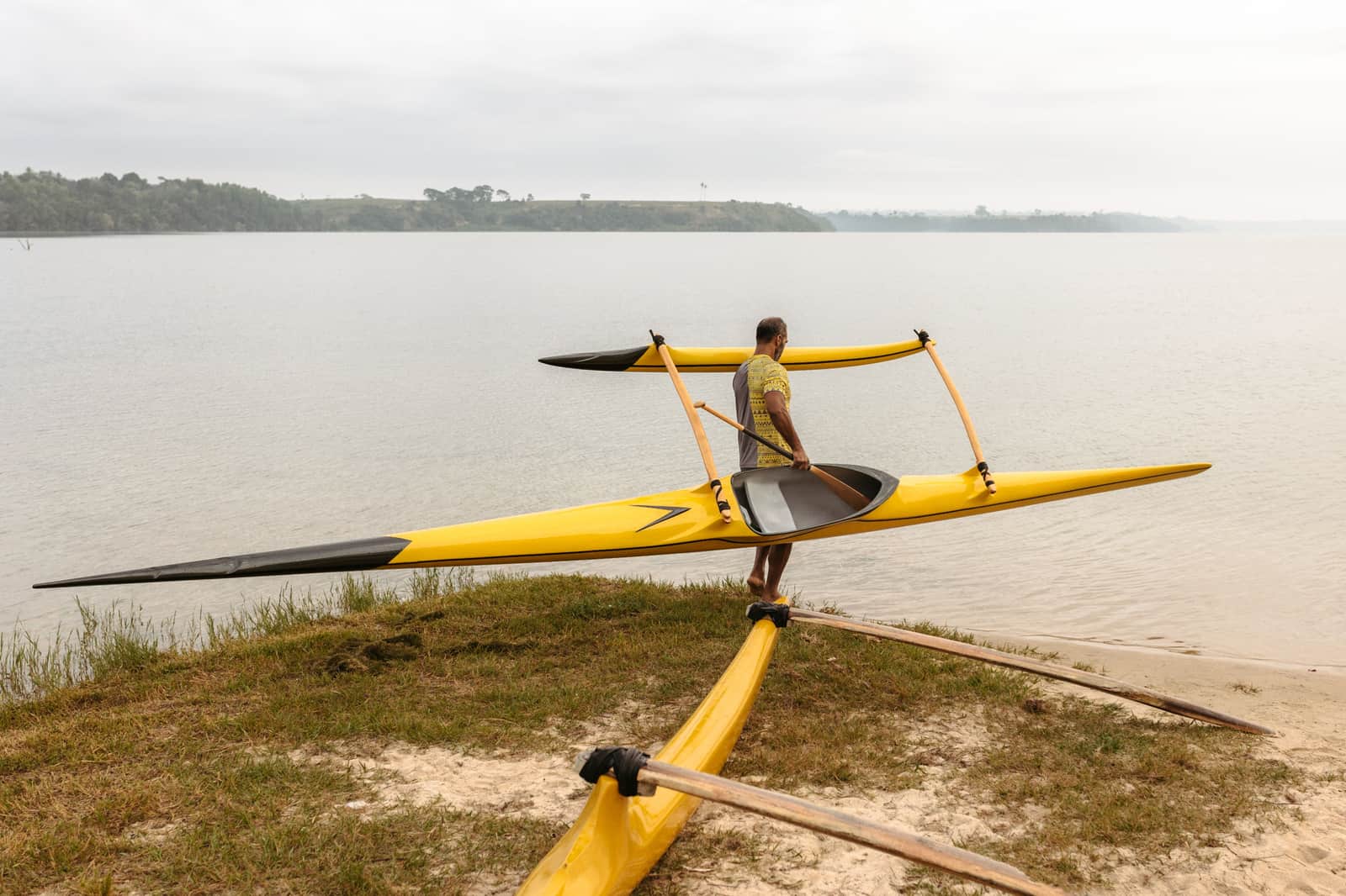 A person carrying a kayak down to the water at a shoreline