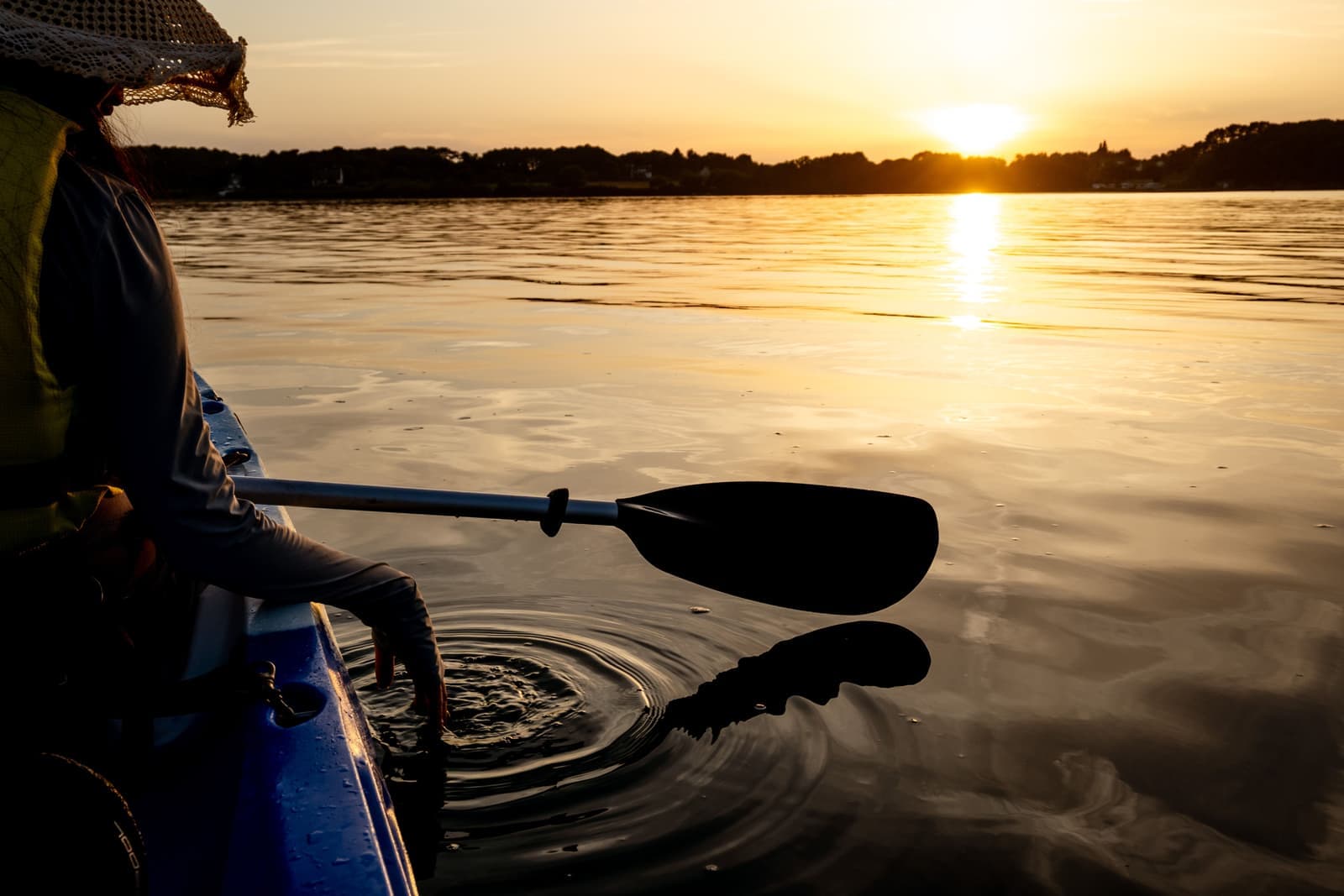 A green recreational kayak on calm water with a paddler aboard