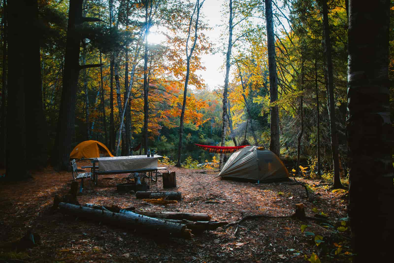 A tent pitched on a shoreline beside a kayak at dusk