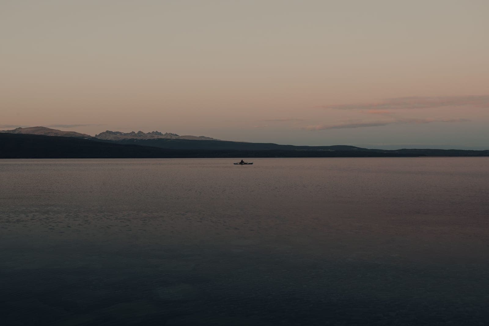 A kayaker crossing a wide flat lake in calm conditions