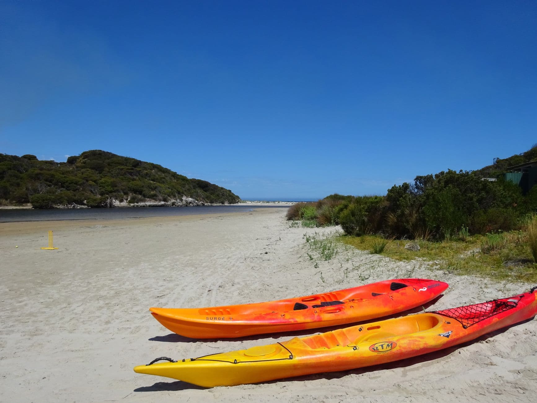Kayaks resting on a quiet sandy beach under a clear sky