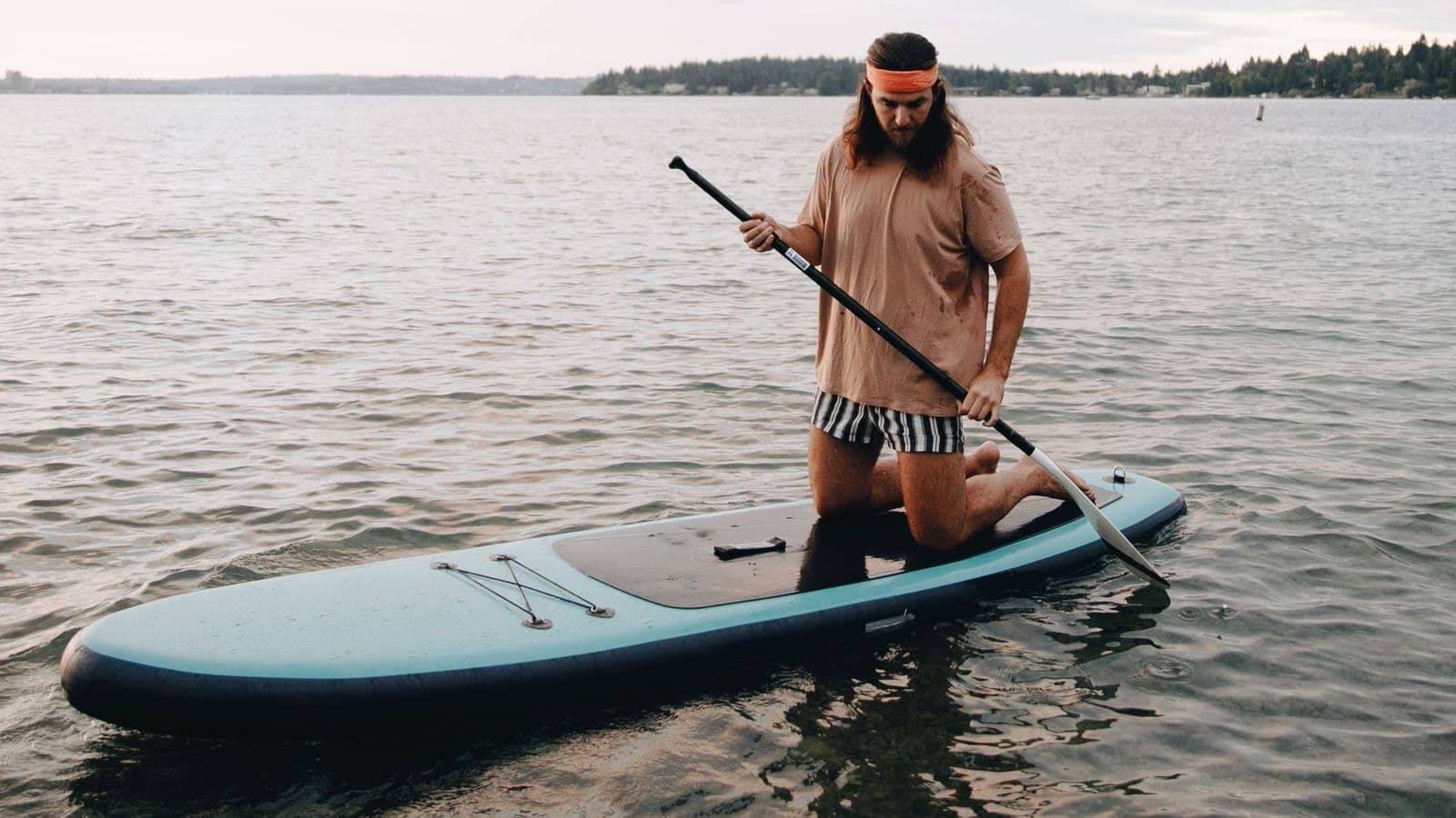 A paddler kneeling on a paddle board on a calm lake