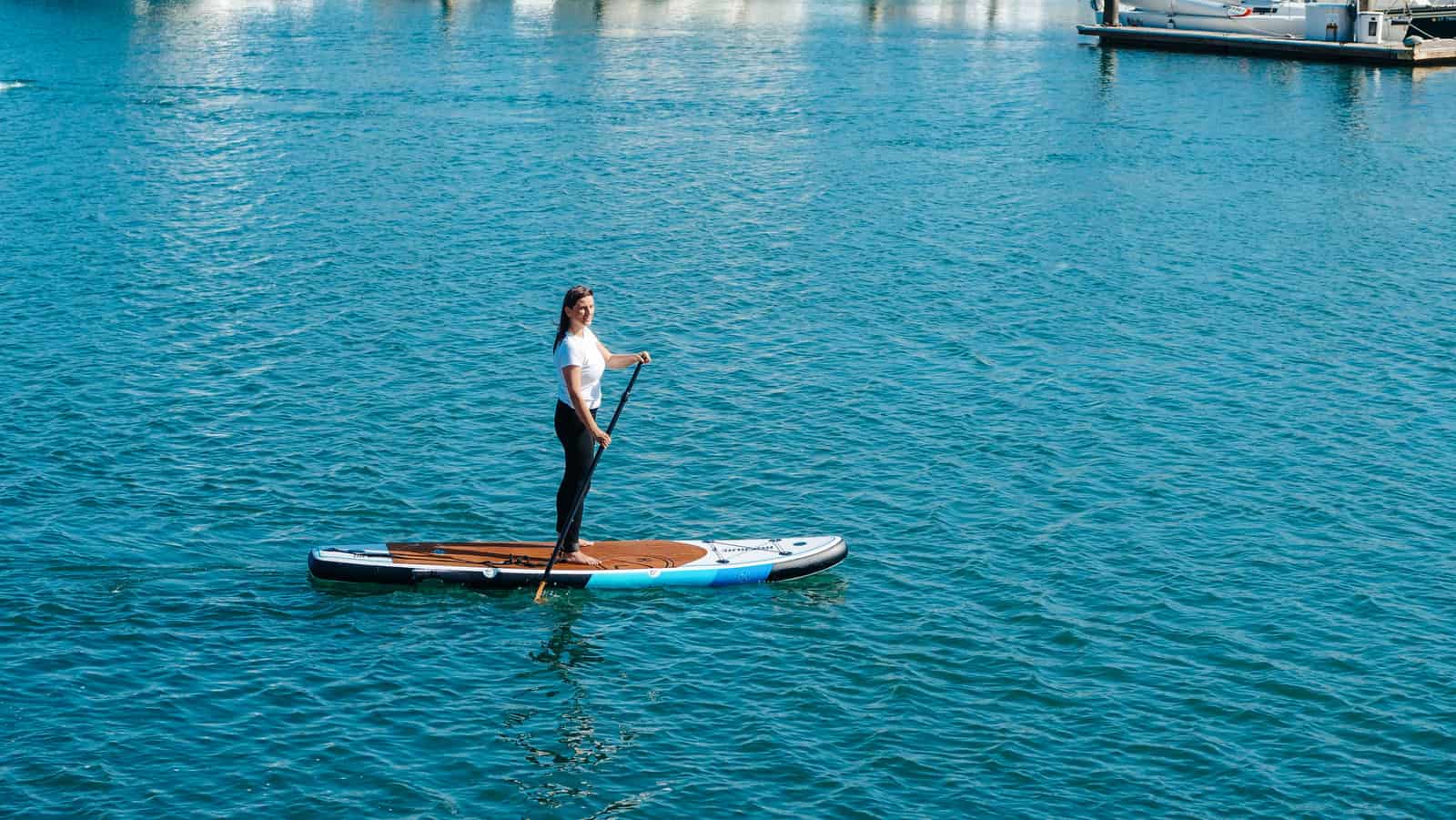 A paddler standing on a wide inflatable board on calm water