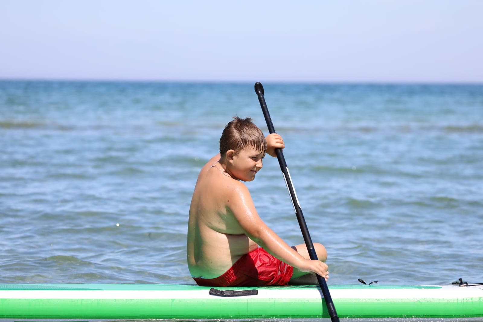 A child kneeling on a paddle board in shallow calm water