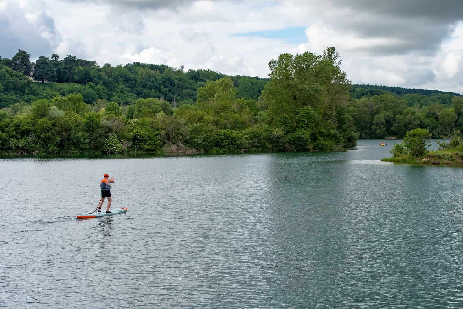 A paddle boarder on a calm river lined with trees
